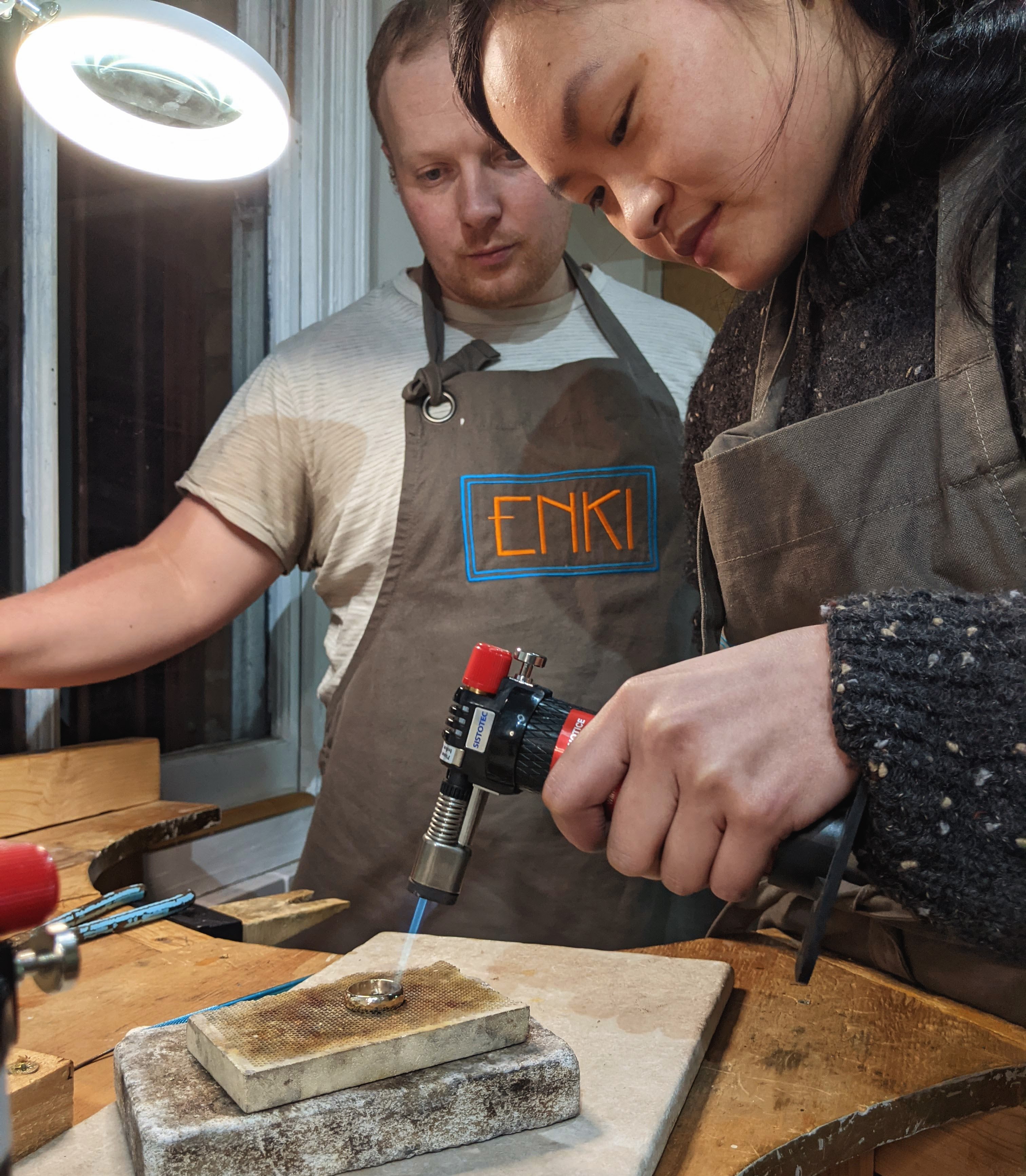 a lady with a blow torch, heating her ring while her partner watches